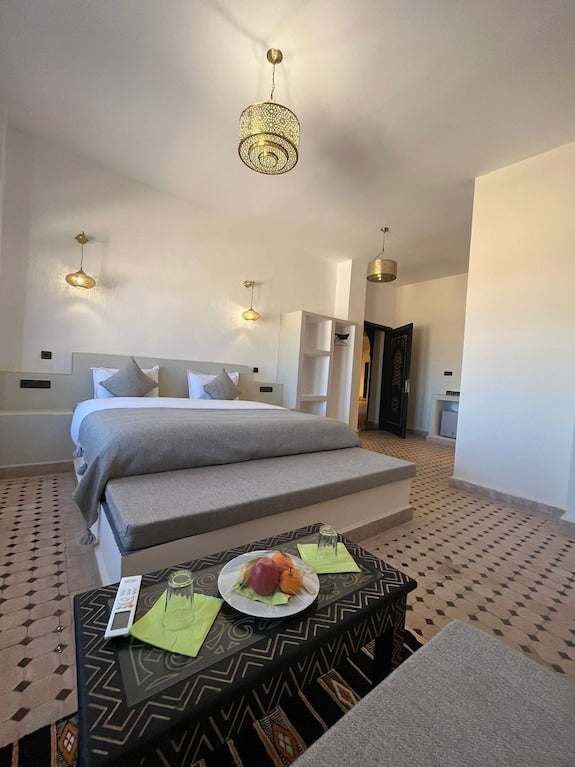 Riad La Luna bedroom with large white bed, patterned tiled floor, modern pendant lights, and a black coffee table with fruit plate