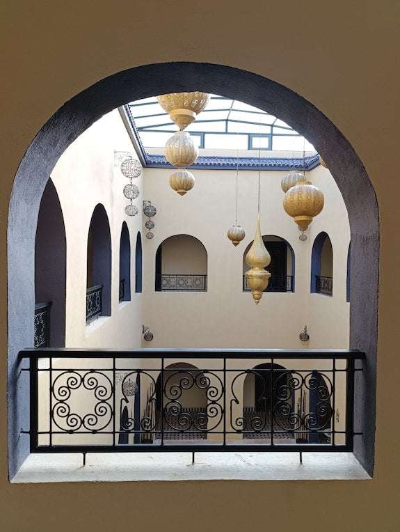 Riad La Luna beige courtyard walls with black wrought iron balcony railings and hanging lanterns architectural details