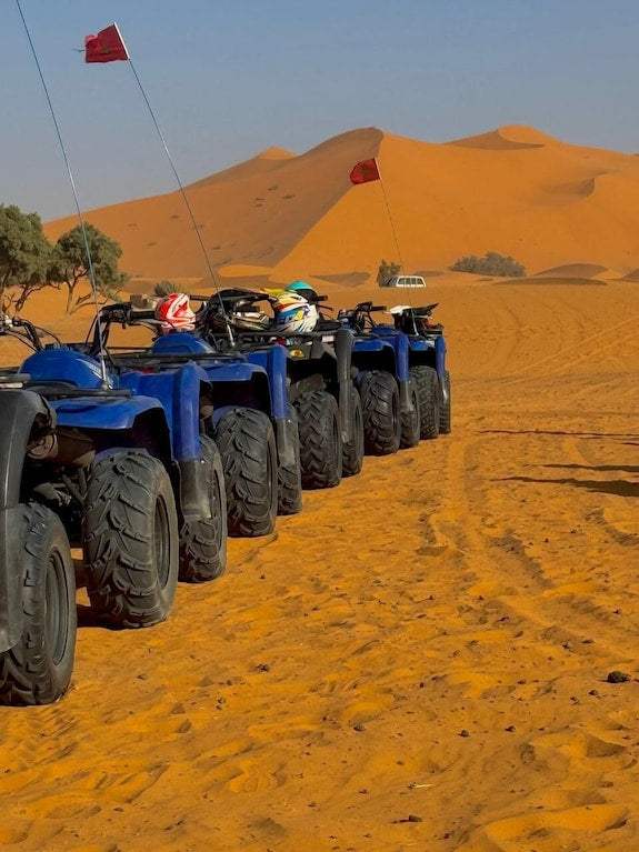 Riad La Luna aligned blue all-terrain vehicles with helmets on orange desert sand near sand dunes under clear sky