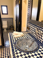Riad La Luna bathroom featuring intricate blue and white mosaic tiles on walls, countertop, and ceramic sink with towel