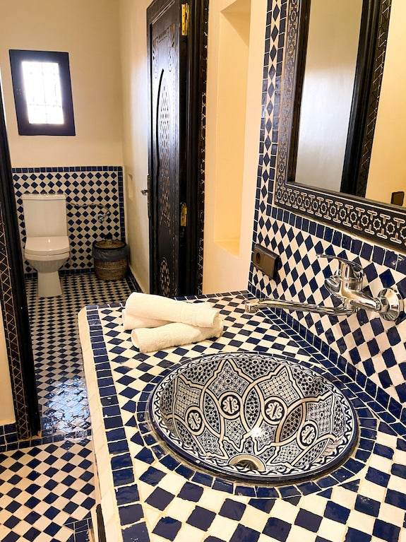 Riad La Luna bathroom featuring intricate blue and white mosaic tiles on walls, countertop, and ceramic sink with towel