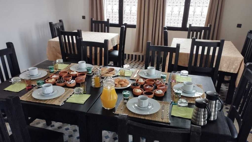 Riad La Luna breakfast setting with black wooden tables and chairs, orange juice, pastries, and small dishes on a patterned floor