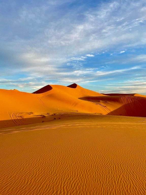 Riad La Luna view of golden sand dunes under blue sky with scattered clouds in Merzouga Morocco desert landscape