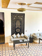 Riad La Luna indoor seating area with beige cushioned sofas, patterned black table, geometric tiled floor, and decorative wall panel