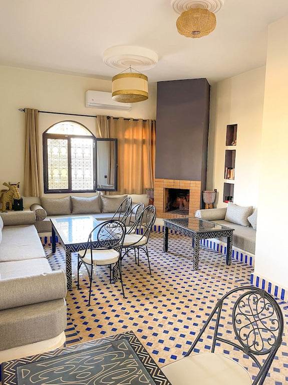 Riad La Luna living room with beige cushions, black wrought iron chairs, patterned tiled floor, and a modern fireplace