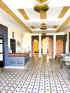 Riad La Luna lobby with beige and blue patterned tiled floor, white walls, arched doorways, and brass hanging lamps