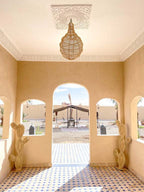 Riad La Luna outdoor archway featuring beige walls, patterned blue and white tile floor, wicker cactus decor, and hanging rattan light