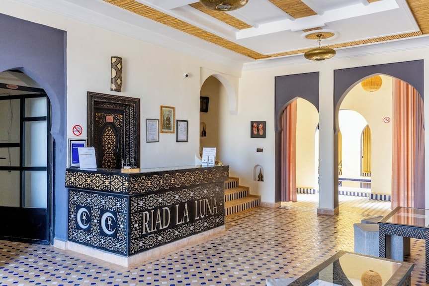 Riad La Luna reception desk with intricate black and gold geometric patterns in bright lobby with arched doorways