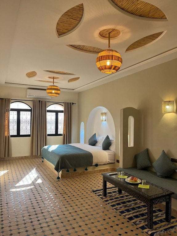 Riad La Luna spacious bedroom in Merzouga Morocco featuring beige walls, patterned tile floor, blue cushions and bedding