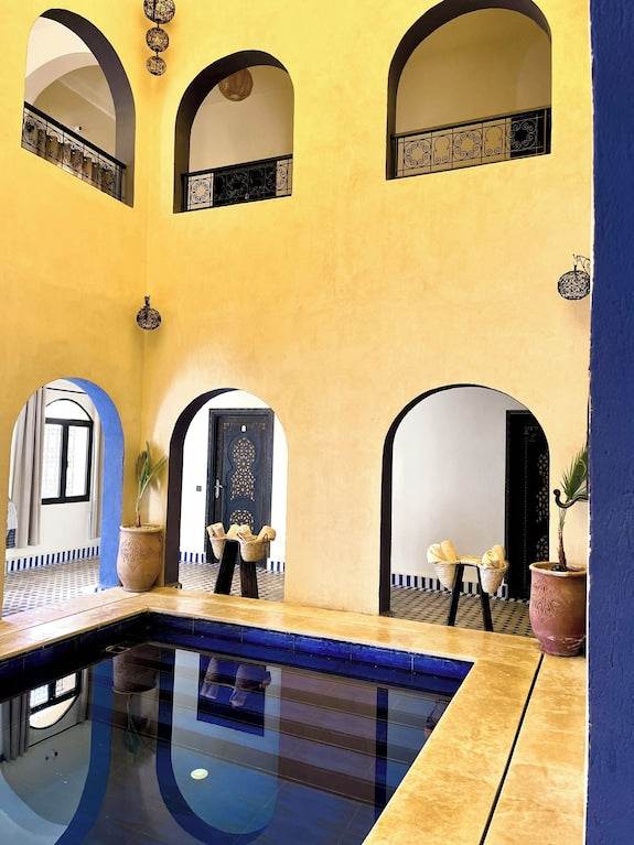 Riad La Luna courtyard with yellow and blue walls featuring arches and a small indoor pool with reflective water