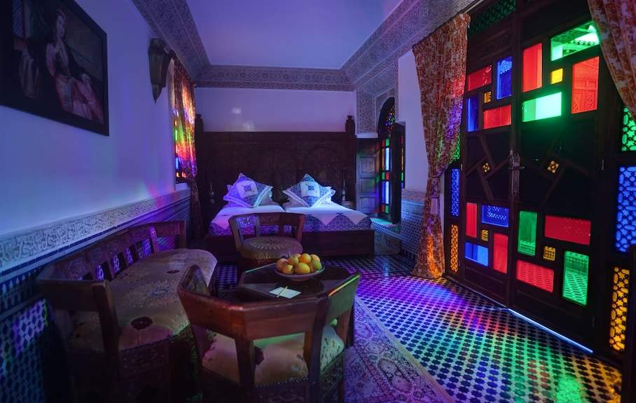 Riad Salam Fes bedroom with double beds, traditional Moroccan wood furniture, patterned tile floor, and colorful stained glass windows