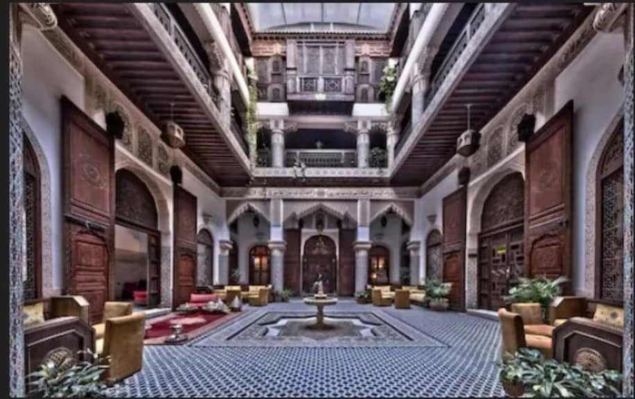 Riad Salam Fes spacious Moroccan courtyard with patterned tile flooring, carved wooden doors, arched design, and seating