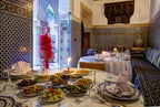 Riad Salam Fes traditional Moroccan dining room with blue and white tilework, patterned cushions, arched doorway, and a table set with colorful dishes and candles
