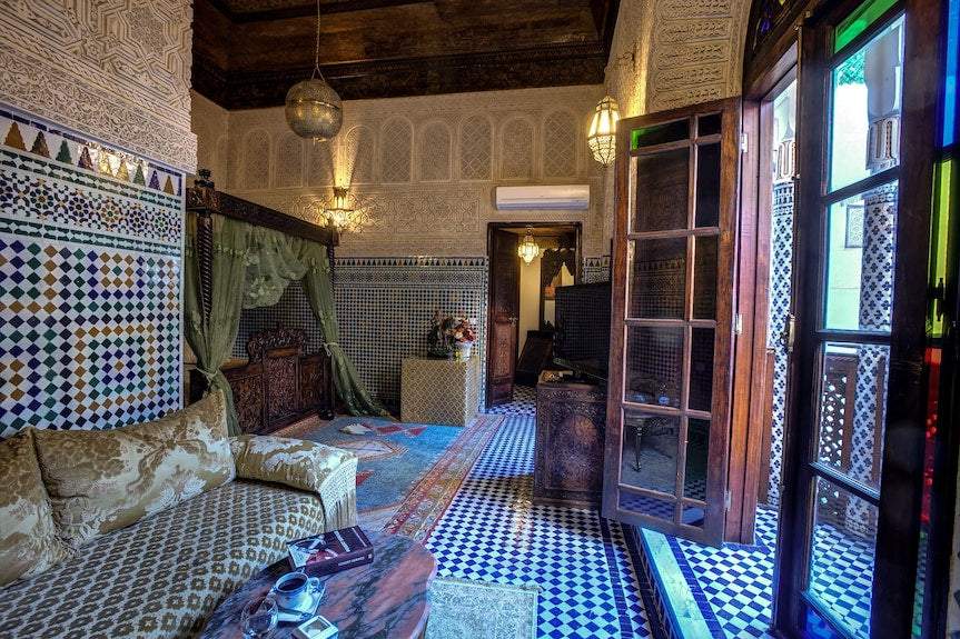 Traditional Moroccan-style room at Riad Salam Fes featuring intricate tilework, carved wood, patterned fabrics, and decorative archways