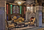 Riad Salam Fes lounge with traditional Moroccan tilework, wooden stained glass windows, ornate columns, vintage upholstered seating, and a tiled fireplace