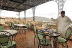 Riad Salam Fes outdoor terrace with green cushioned wrought iron chairs, tiled floor, and man serving tea under ornate canopy