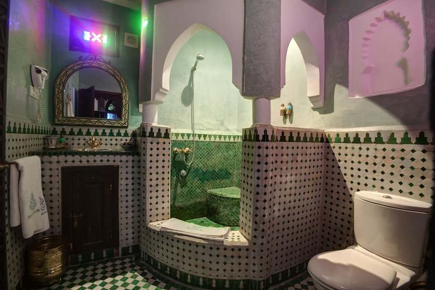 Traditional Moroccan bathroom at Riad Salam Fes with green and white mosaic tiles, arch design, shower, and toilet