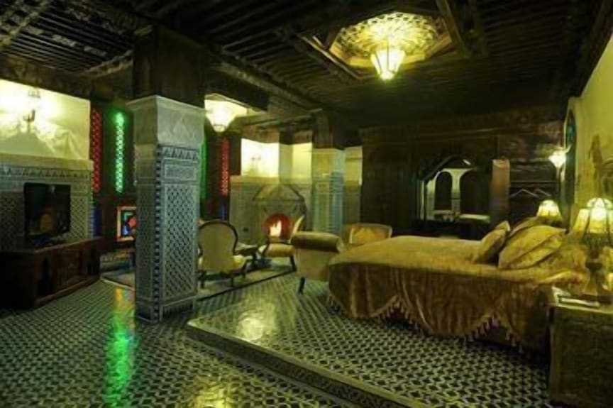 Riad Salam Fes bedroom featuring traditional Moroccan decor, intricate tiled floors, carved wood ceilings, and luxurious bedding