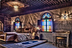 Riad Salam Fes bedroom with traditional Moroccan wooden ceiling, colorful stained glass windows, ornate patterned walls, and a plush bed with decorative pillows and textiles