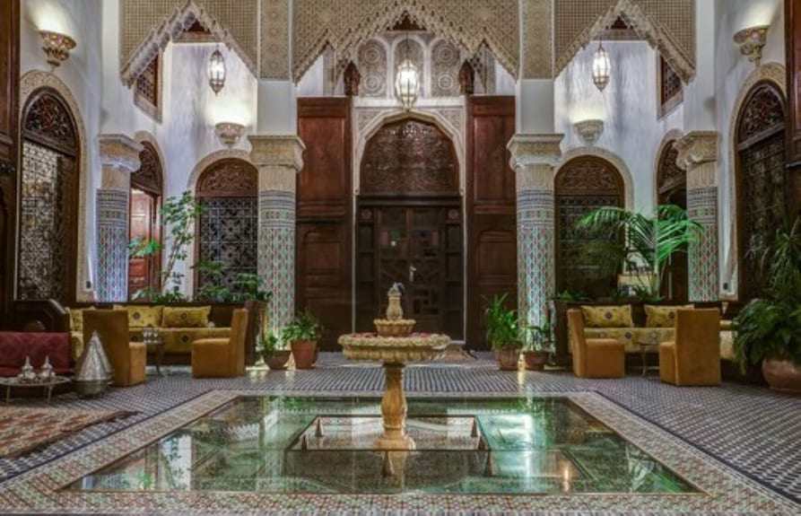 Riad Salam Fes interior courtyard with traditional Moroccan arches, intricate tilework, central fountain, and plush seating