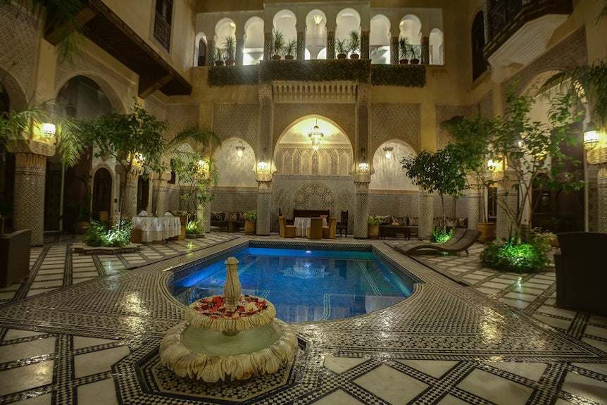 Riad Salam Fes featuring a traditional Moroccan courtyard with mosaic tiled floor, fountain, small pool, arched colonnades, and lantern lighting