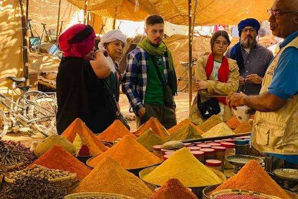 Outdoor market stall with colorful spice cones in shades of yellow, orange, and red, surrounded by people in traditional attire during the Rissani Market Day Tour.