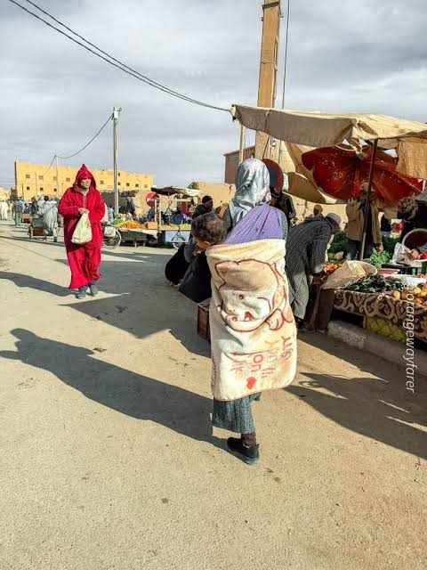 Outdoor market scene at Rissani with local people wearing traditional robes, colorful textiles, and vendors selling goods on Rissani Market Day Tour
