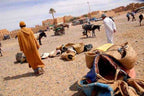 Outdoor market scene with woven baskets and rugs on rocky ground, two men walking and donkeys nearby during Rissani Market Day Tour.