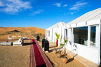 Royal Desert Camp with white canvas tents, large windows, outdoor seating, potted plants, and a red carpet walkway in the desert.
