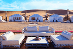 Luxury outdoor seating area with white cushions and low wooden tables in front of white canvas tents at a Royal Desert Camp in the desert.