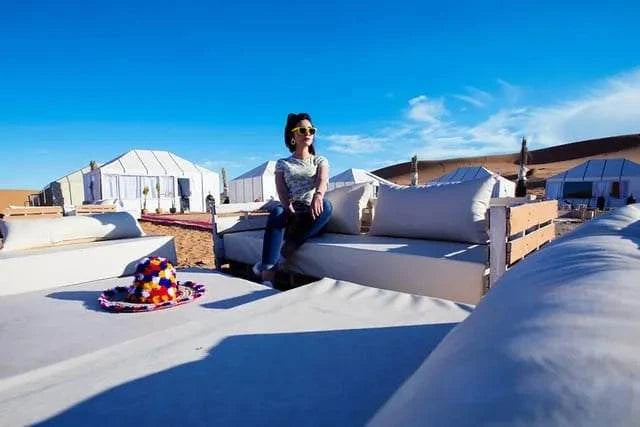 Royal Desert Camp outdoor seating area with white cushioned sofas, beige fabric, and desert tents under a blue sky.