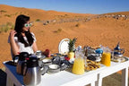 Outdoor breakfast setup at a Royal Desert Camp featuring black and white patterned ceramic dishes, fresh juice, and traditional Moroccan teapots in the Sahara sand dunes.