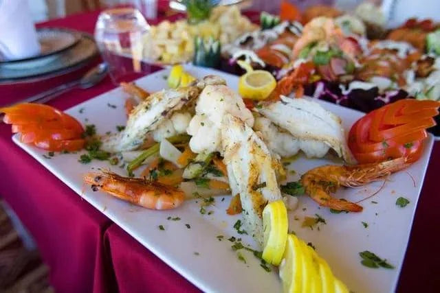 Seafood platter with grilled fish, shrimp, lemon wedges, and garnishes served on a white plate with decorative tomato slices, representing Royal Desert Camp cuisine.