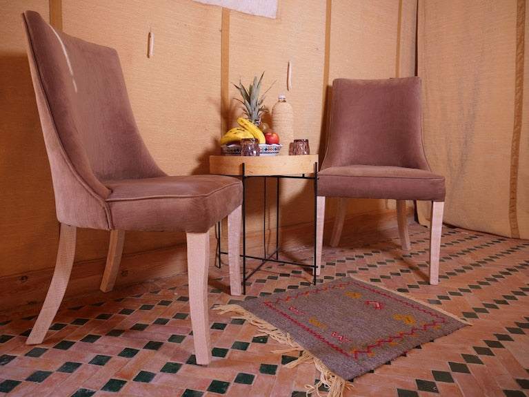 Royal Luxury Camp seating area with two brown upholstered chairs, a small black metal table with fruit, and a patterned floor mat