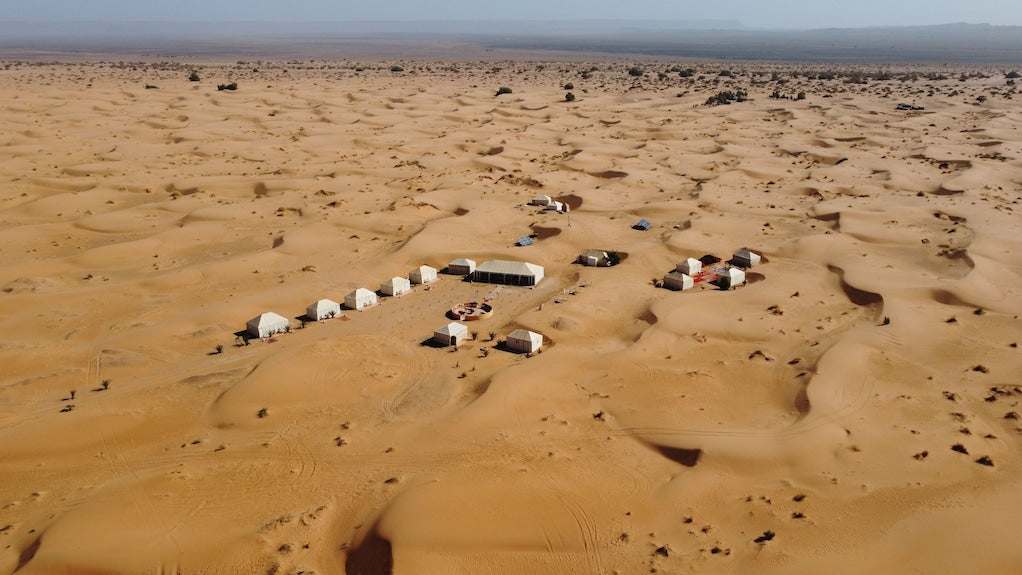 Royal Luxury Camp aerial view showing beige luxury tents arranged in a desert with sandy dunes and sparse vegetation