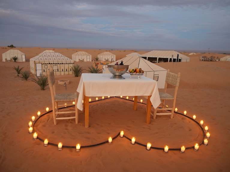 Royal Luxury Camp outdoor dining setup with wooden table and chairs surrounded by heart-shaped candles on desert sand