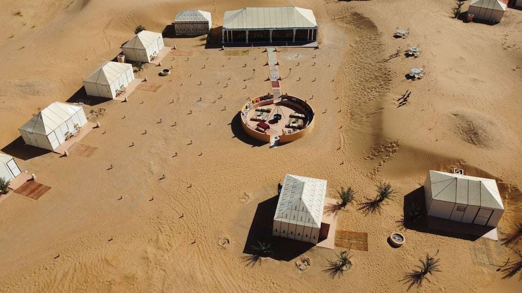 Royal Luxury Camp aerial view showing white canvas tents with rectangular shapes arranged in desert sand with seating area in center