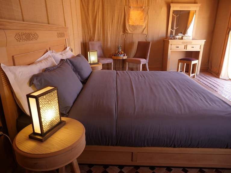 Royal Luxury Camp bedroom with wooden frame bed, gray bedding, bedside lamps, and wooden furniture in warm tones