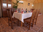 Royal Luxury Camp wooden dining table with white tablecloth, blue patterned dinnerware, wine bottles, and wooden chairs inside a beige tented room