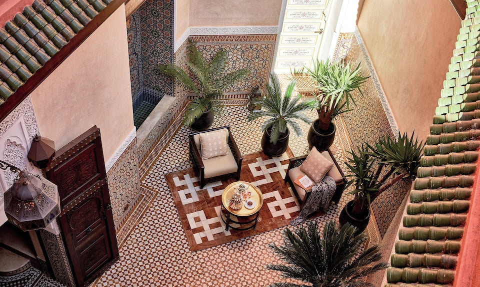 Royal Mansour Marrakech courtyard with ornate Moroccan tilework, potted plants, woven rug, and cushioned seating around a tea table
