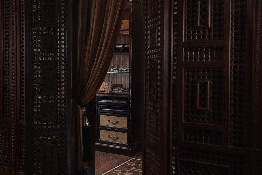 Dark wooden carved doors partially open to a room with traditional Moroccan design and woven baskets inside, evoking Royal Mansour Marrakech
