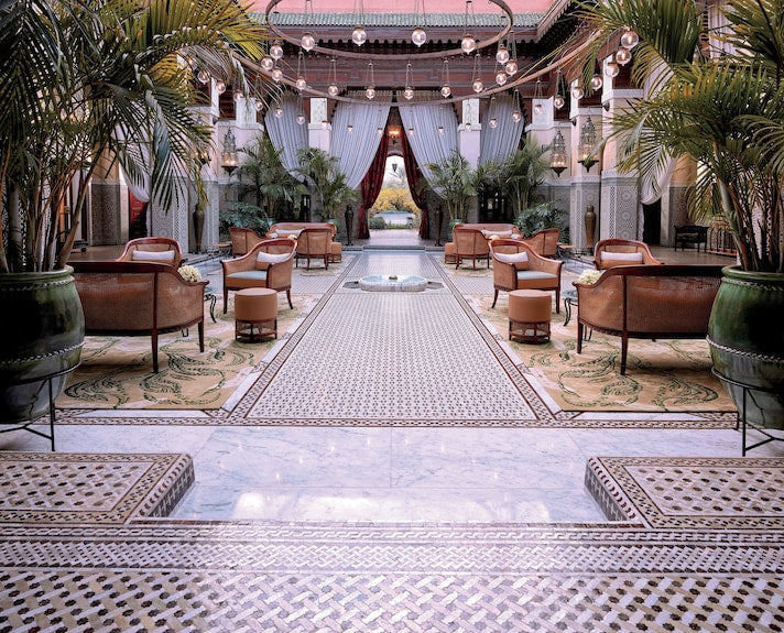 Royal Mansour Marrakech courtyard with intricate mosaic tile flooring, elegant brown leather chairs, palm plants, and hanging lanterns