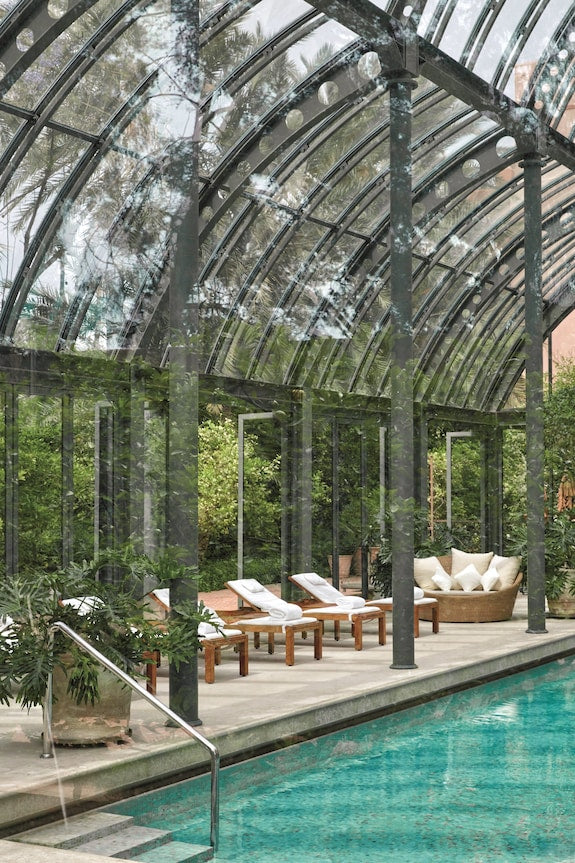 Royal Mansour Marrakech indoor pool area with glass ceiling, green metal framing, cushioned loungers, and tropical plants