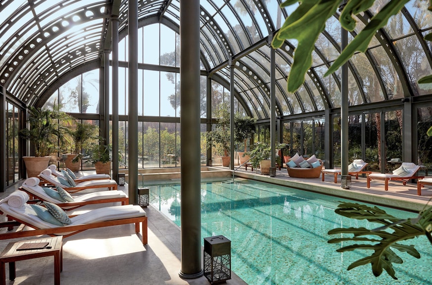 Royal Mansour Marrakech indoor pool with turquoise tiles, wooden lounge chairs with white cushions, and glass dome roof