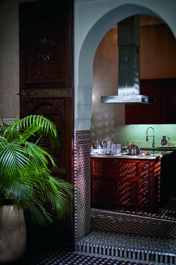 Royal Mansour Marrakech kitchen space featuring dark wood cabinetry with intricate geometric patterns, traditional Moroccan tilework, and a green indoor plant