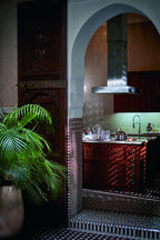 Royal Mansour Marrakech kitchen space featuring dark wood cabinetry with intricate geometric patterns, traditional Moroccan tilework, and a green indoor plant