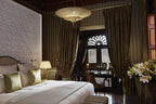 Luxury bedroom at Royal Mansour Marrakech featuring an ornate white carved wall, large bed with green and white pillows, dark patterned curtains, and elegant lighting