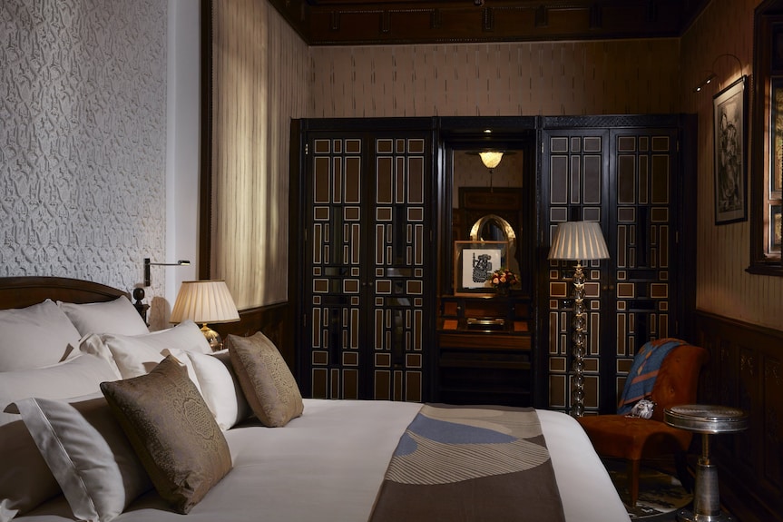Luxury bedroom at Royal Mansour Marrakech featuring white bedding, brown cushions, intricate wood paneling, and ornate dark doors