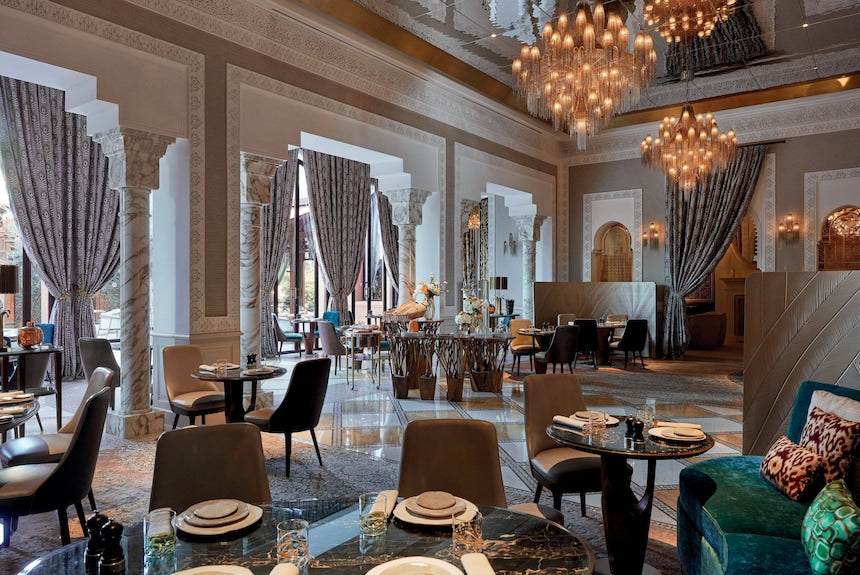 Luxury dining area at Royal Mansour Marrakech featuring elegant dark wood furniture, marble floors, intricate arches, and grand chandeliers