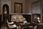 Luxury living room at Royal Mansour Marrakech featuring beige patterned sofa, wooden tables, lit fireplace with intricate tilework, and Moroccan decor